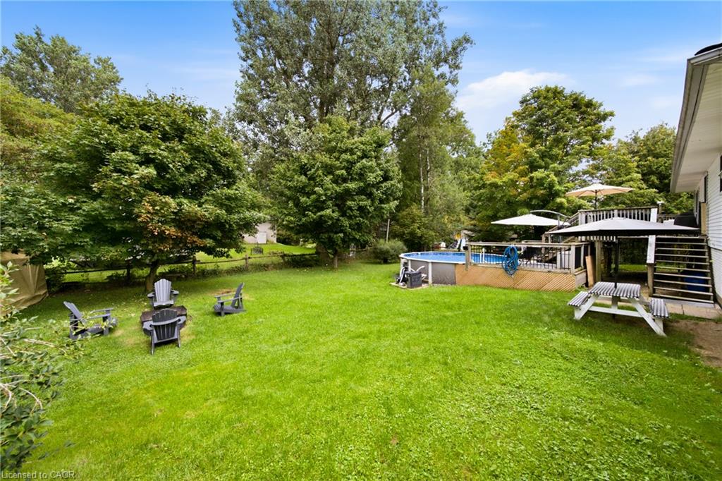 Backyard with a lawn, mature trees, Adirondack chairs, above-ground pool, and raised deck.