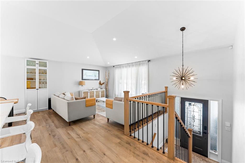 Furnished living room with light sofas, wood floors, and a starburst pendant beside the open stairwell.
