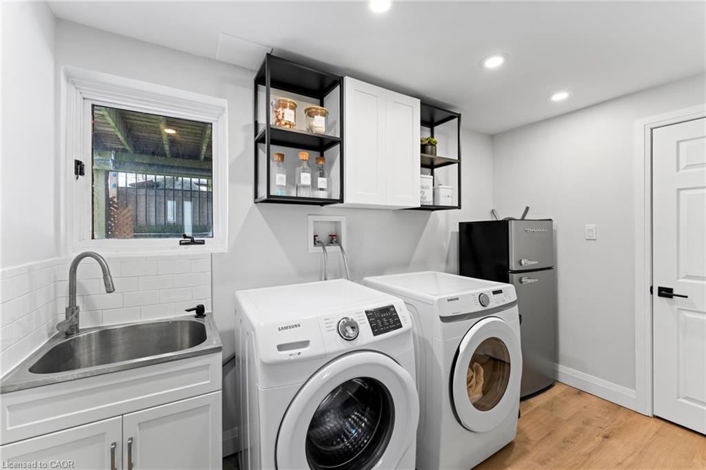 Laundry room with front-loading washer and dryer, utility sink, open shelves, and compact refrigerator.