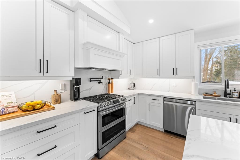 White kitchen with a stainless-steel gas range, marble-look counters, and a window above the sink.