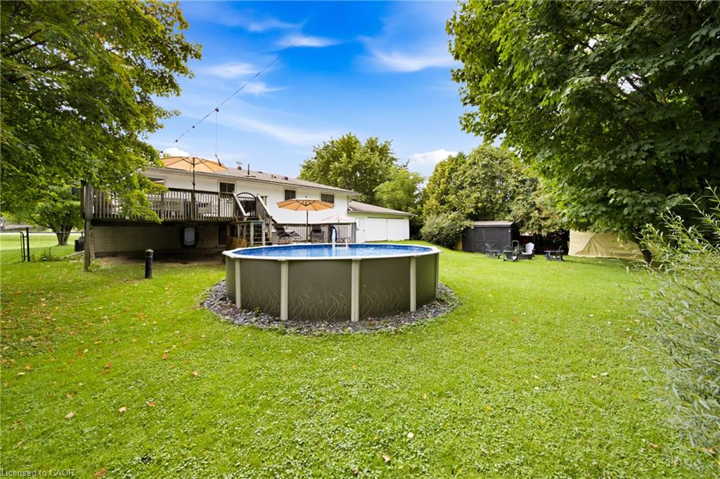 Backyard with a round above-ground pool, raised deck, and broad green lawn.