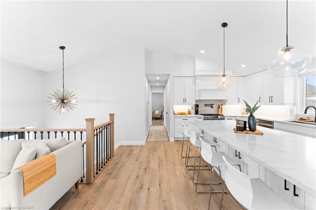 Open-plan kitchen with a large white island, bar stools, and light wood flooring beside a living area.
