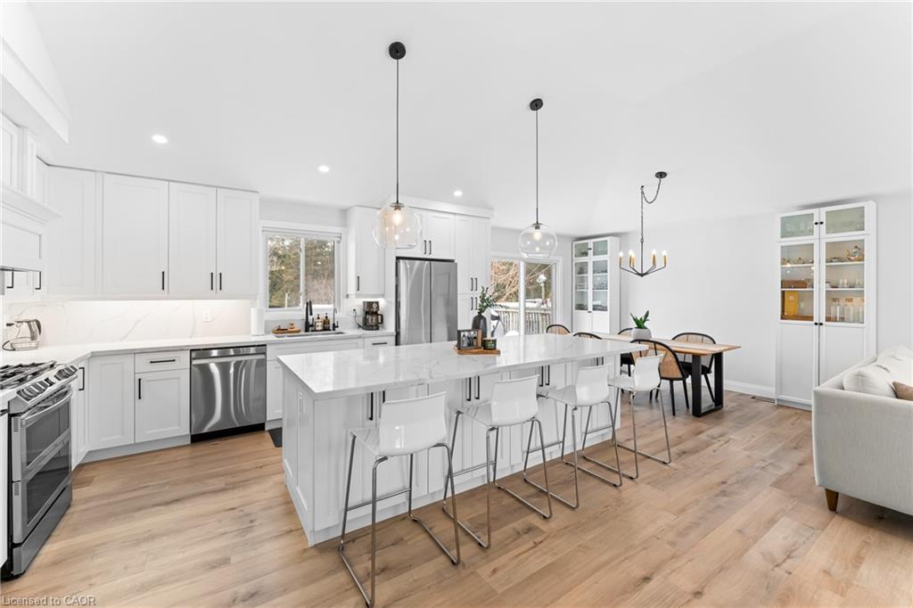 Bright white kitchen with a large island, stainless steel appliances, and an adjoining dining area.