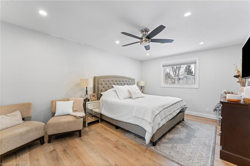 Bedroom with a tufted bed, upholstered chairs, ceiling fan, and light wood floors.