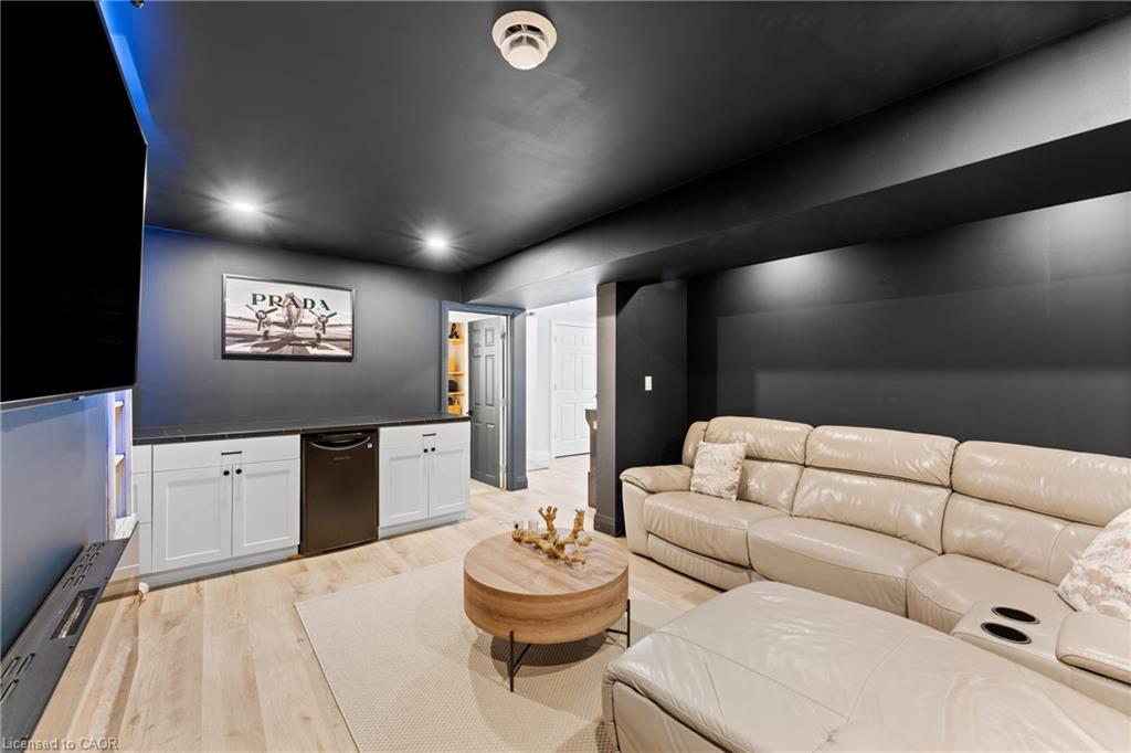 Media room with a beige sectional, large television, white cabinets, and round coffee table.