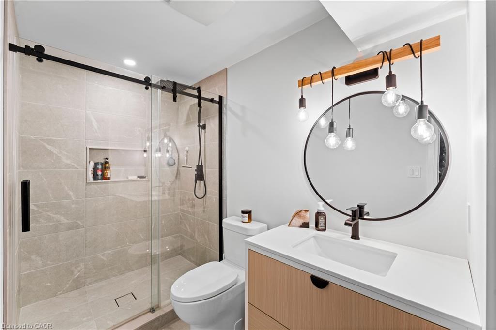 Modern bathroom with a tiled glass shower and wood-front vanity beneath a round mirror.
