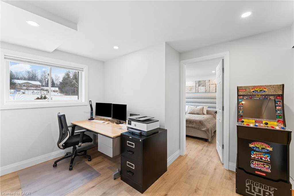 Home office with a desk and dual monitors, snowy yard outside, and an arcade game beside the bedroom doorway.