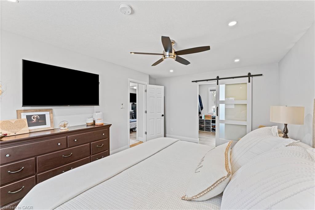 Staged bedroom with white bedding, a dark wood dresser, and a sliding frosted-glass barn door.