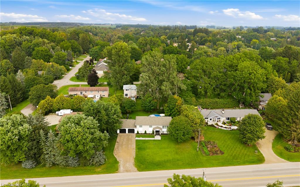 Aerial view of a home with a gravel driveway, broad lawn, and pool behind it.