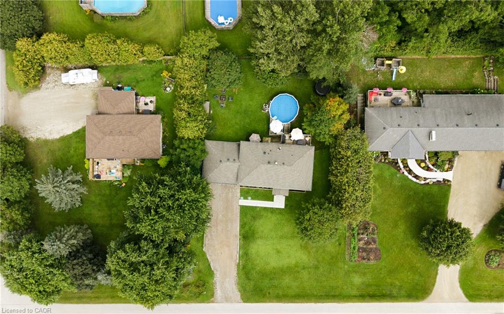 Aerial view of a house surrounded by lawn and mature trees, with a driveway and above-ground pool.