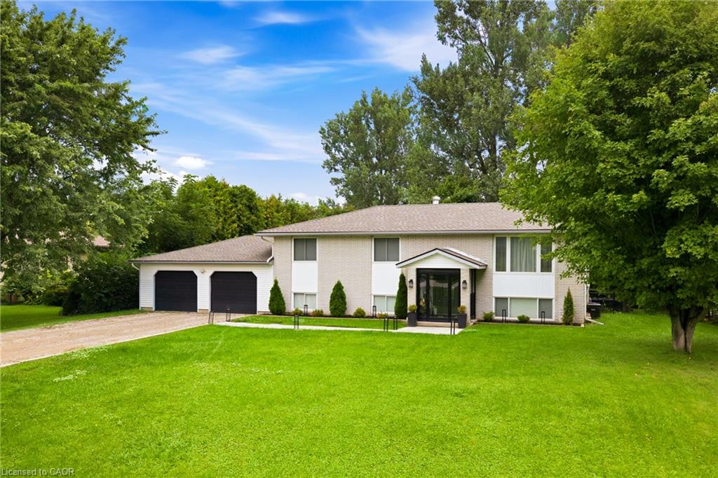Split-level house with an attached two-car garage, covered glass entry, and broad green lawn.