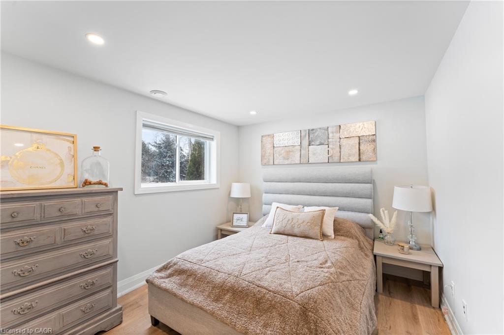 Staged bedroom with a beige quilted bed, gray upholstered headboard, and window overlooking trees.