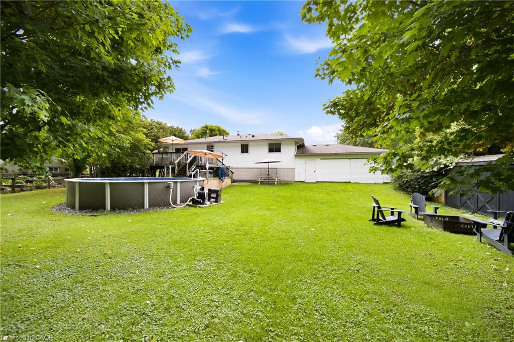Backyard with a broad lawn, above-ground pool, raised deck and mature trees.