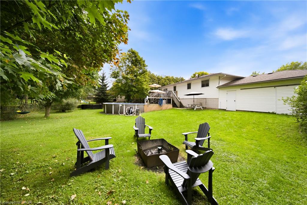 White house and backyard with an above-ground pool, deck, and chairs around a fire pit.