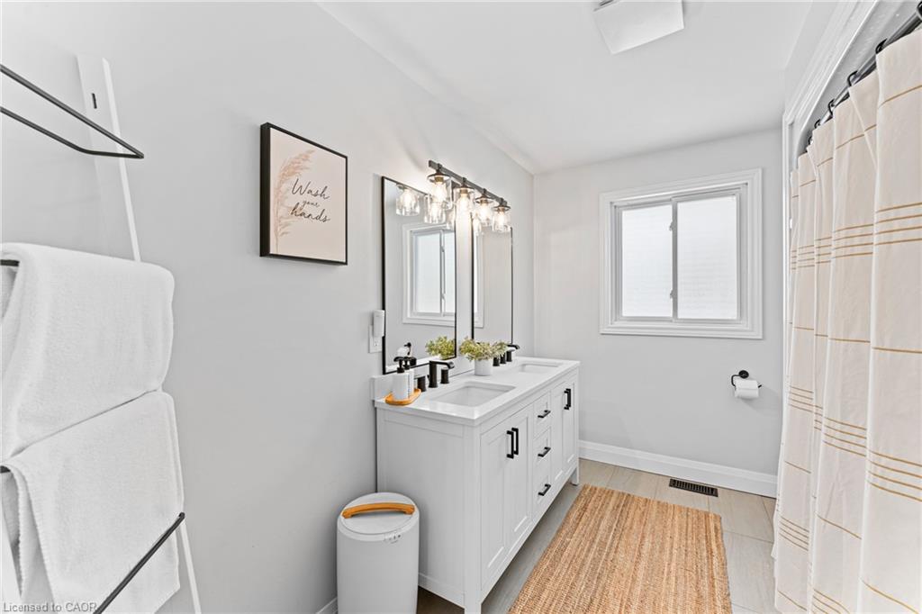 Bright bathroom with a white double vanity, black fixtures, and a window beside a striped shower curtain.