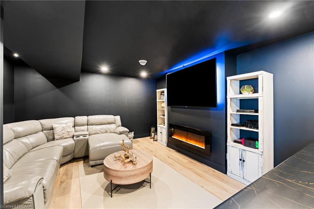 Media room with a white sectional, wall-mounted TV, blue accent lighting, and electric fireplace.