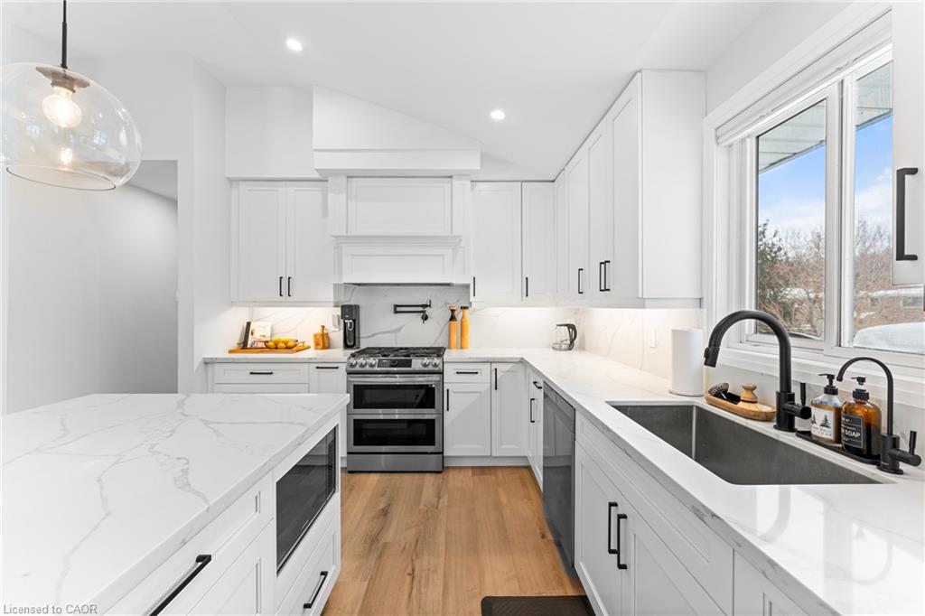 White kitchen with a marble-look island, stainless steel range, wood floors, and a large window above the sink.