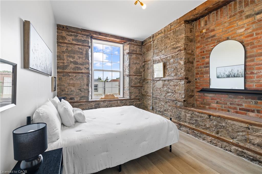 Bedroom with a white bed, exposed stone and brick walls, and a large window.