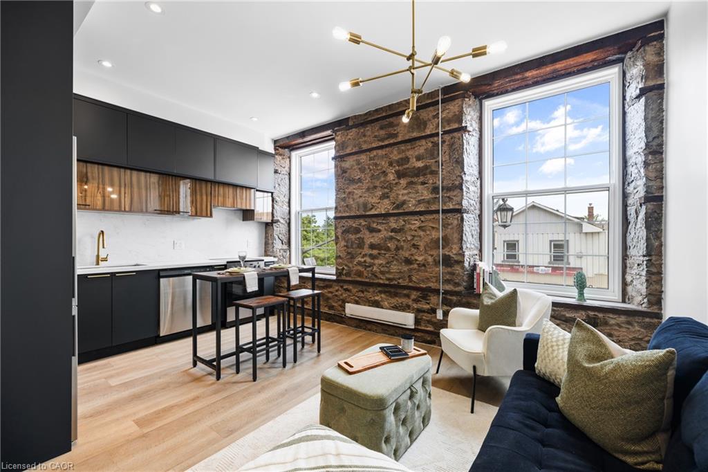 Open-plan living room and kitchen with exposed stone walls, tall windows, and dark cabinetry.