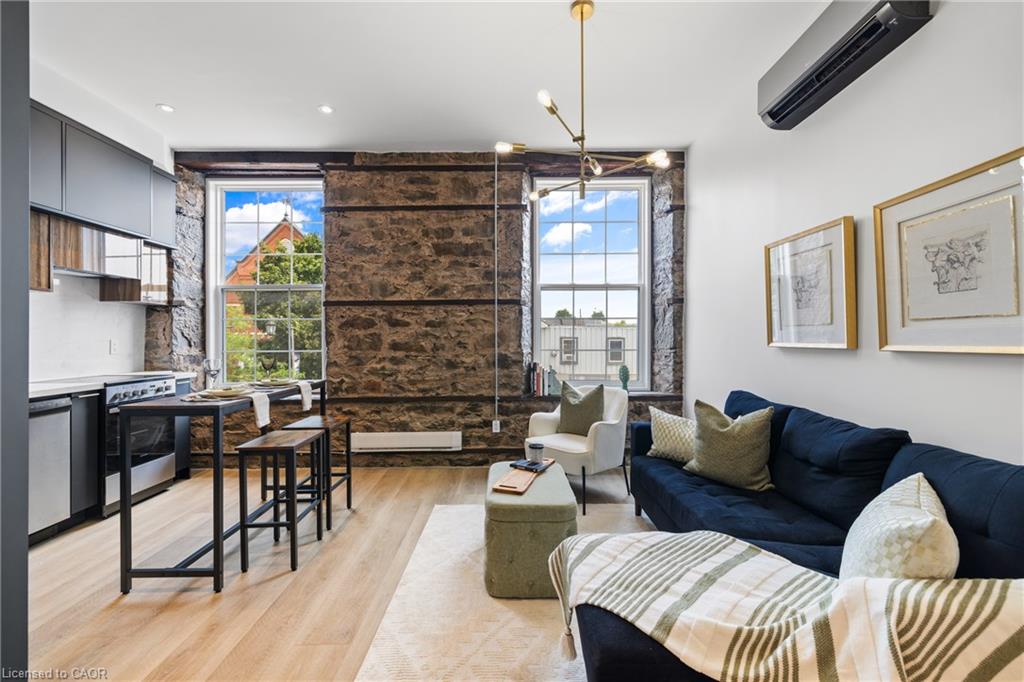 Open-plan condo living room with exposed stone walls, tall windows, and a dark blue sectional sofa.