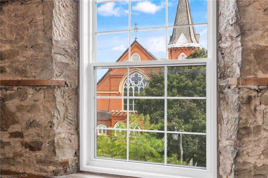 Stone interior wall and window overlooking a red-brick church steeple and leafy trees.