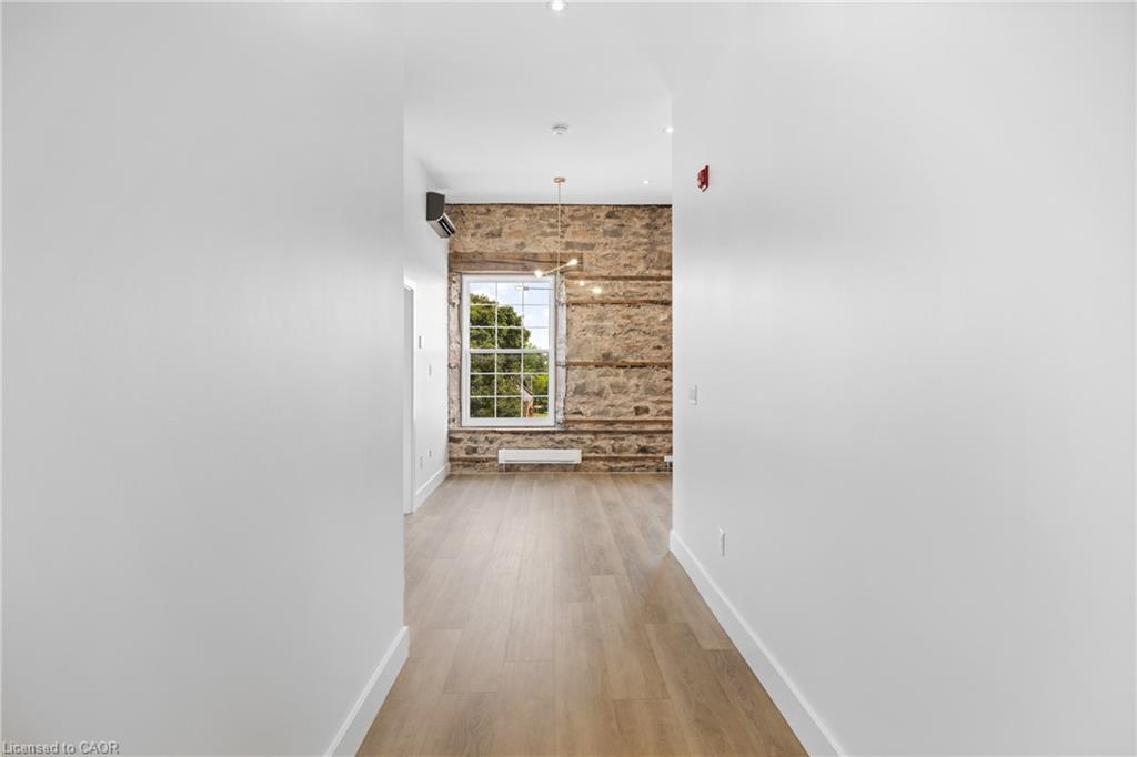 Empty apartment hallway opening onto a room with a stone accent wall and large window.
