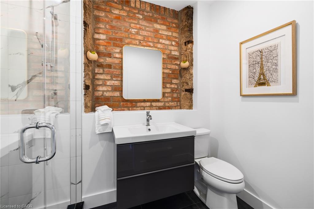 Bathroom with a dark floating vanity, glass shower, and exposed brick wall behind the mirror.