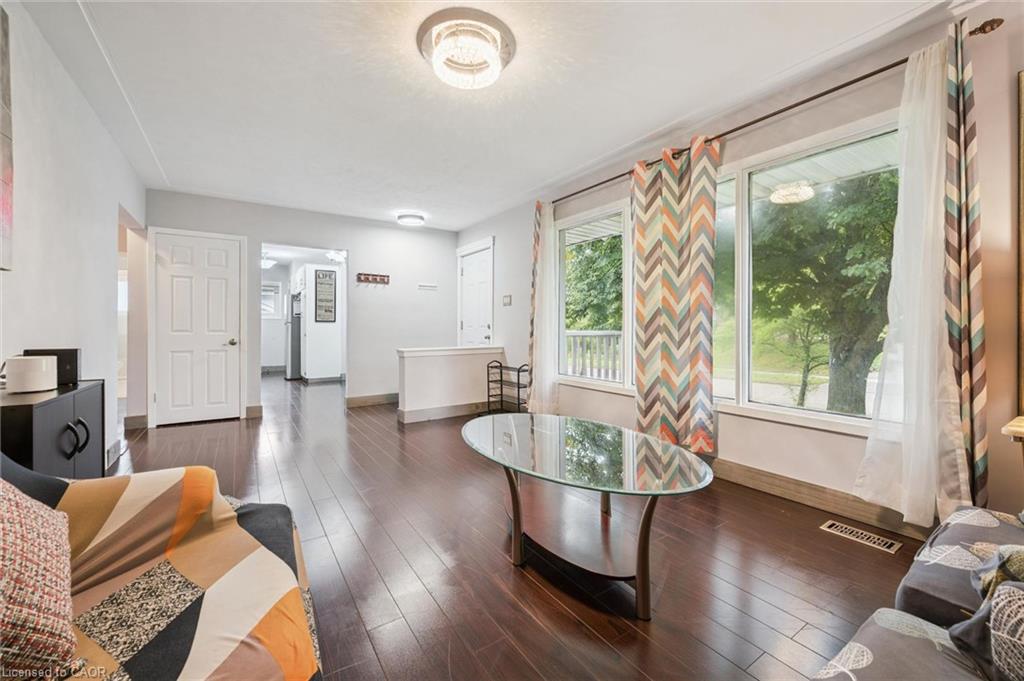Furnished living room with dark hardwood floors, a glass coffee table, and chevron curtains beside large windows.