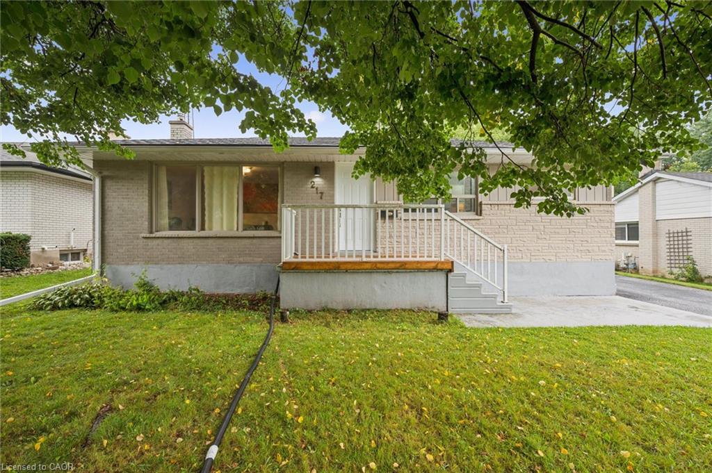 Single-story brick home with a raised white-railed porch beneath mature trees.