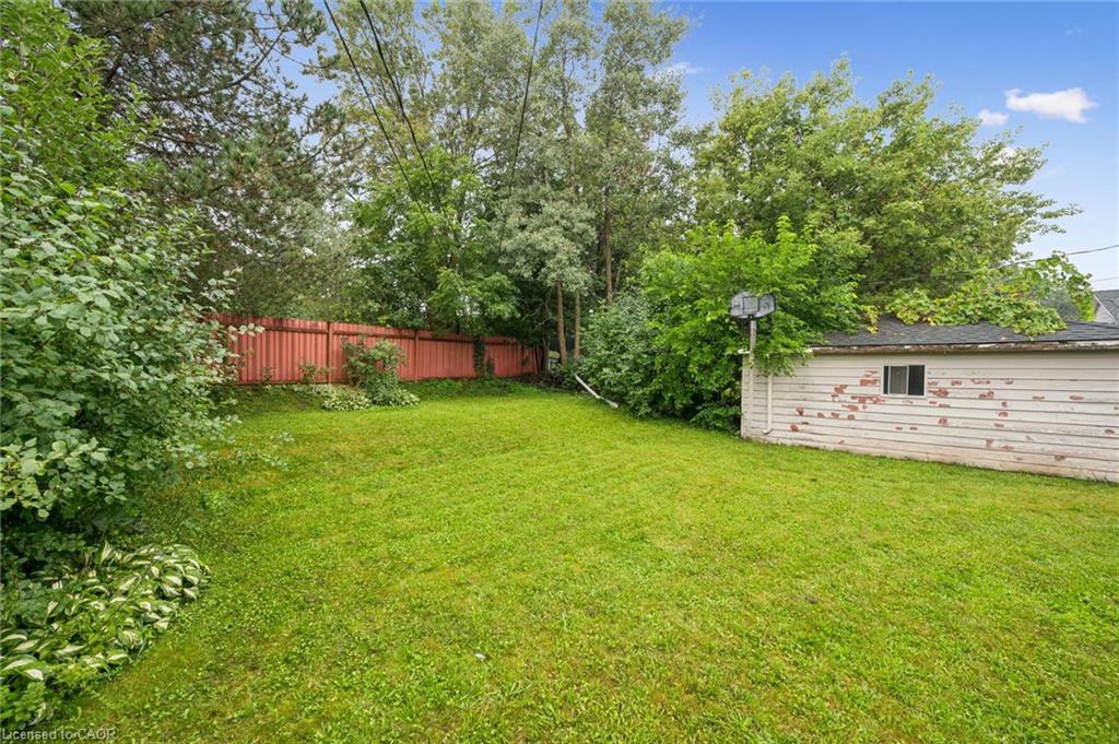 Grassy backyard with mature trees, a red fence, and a detached garage.