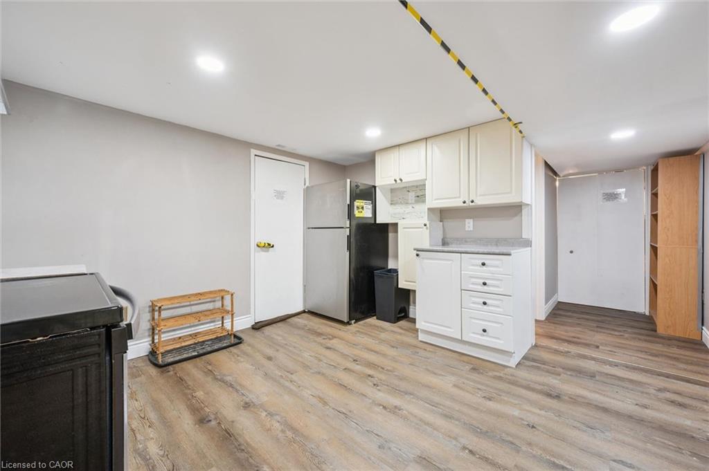 Basement kitchenette with white cabinets, refrigerator, and wood-look flooring.
