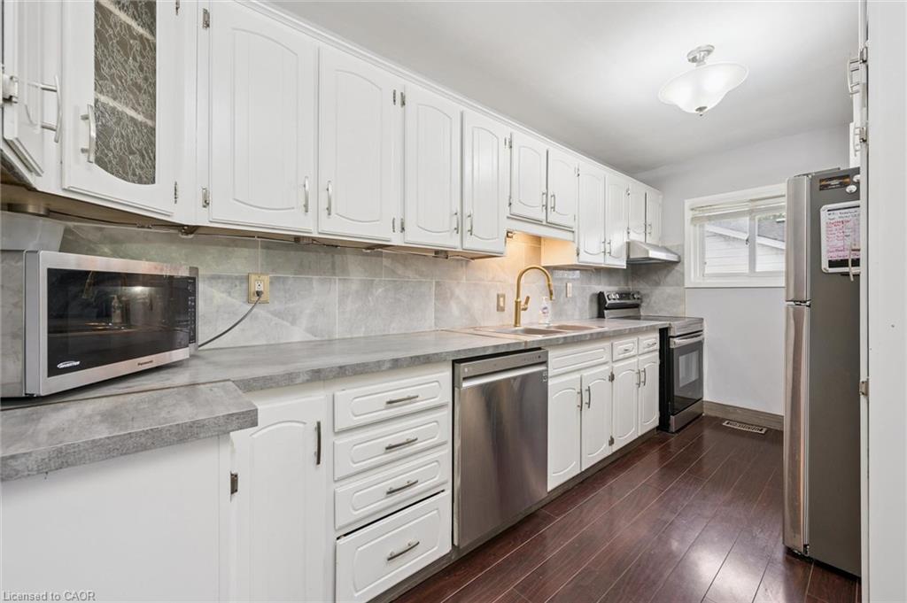 Kitchen with white cabinetry, stainless steel appliances, gray counters, and dark flooring.