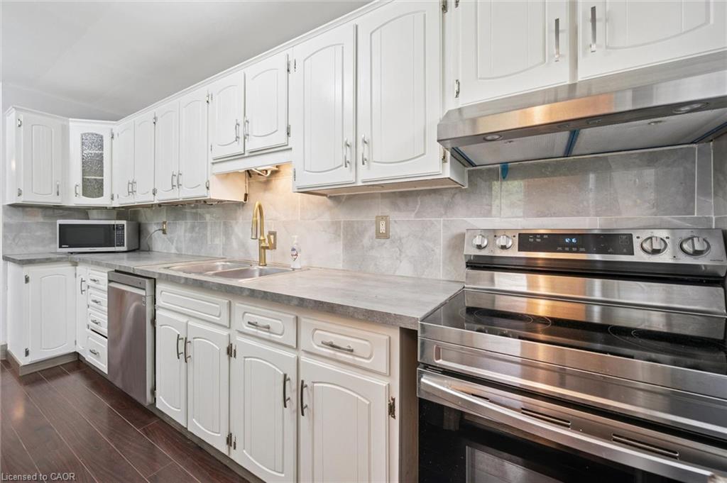 Kitchen with white cabinets, gray counters, stainless steel appliances, and a gold-tone faucet.