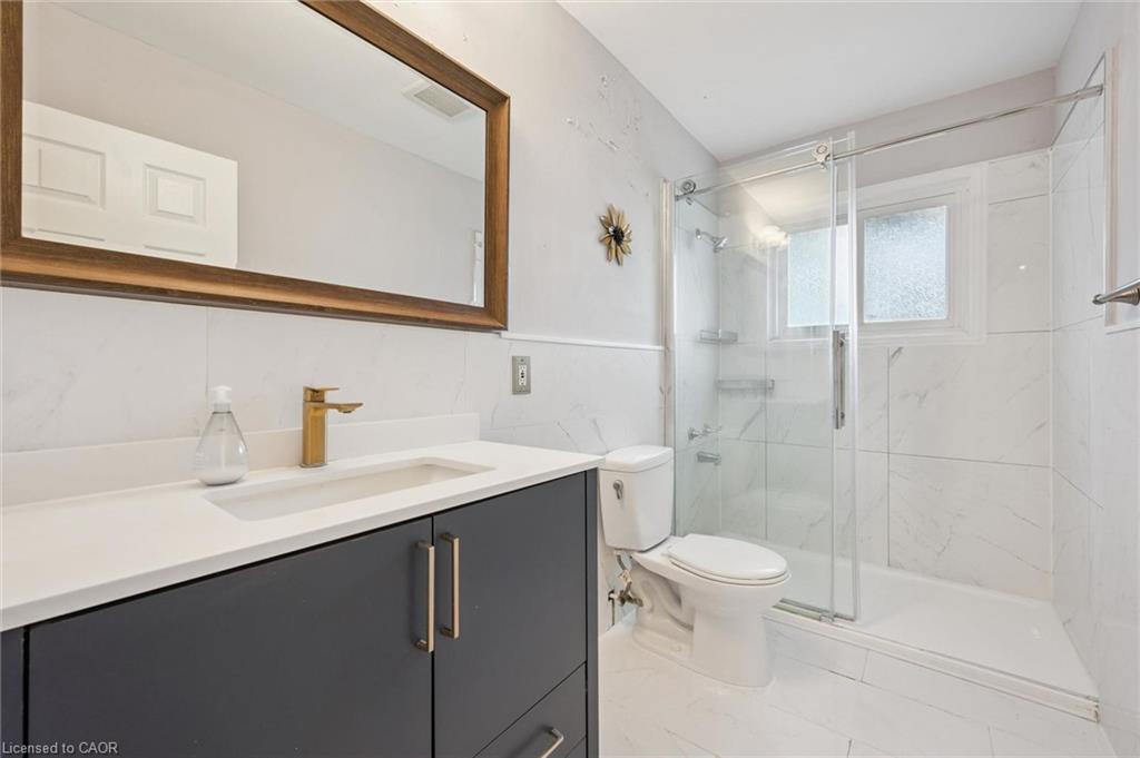 Bathroom with a dark gray vanity, gold faucet, and glass-enclosed shower.
