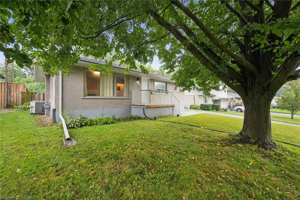 Single-story brick house with a raised porch, framed by a large shade tree and front lawn.