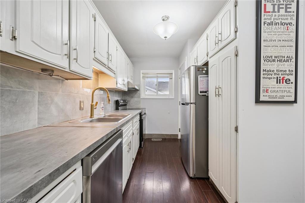 Galley kitchen with white cabinets, gray counters, a brass faucet, stainless-steel appliances, and dark flooring.