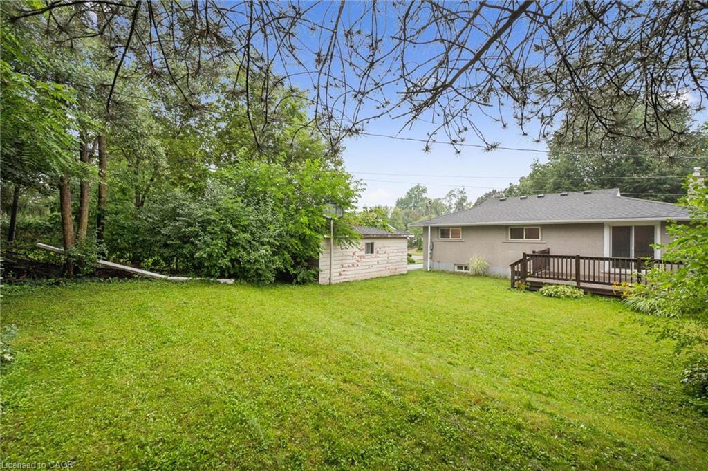 Grassy backyard with mature trees, a small shed, and a raised deck behind a single-story home.