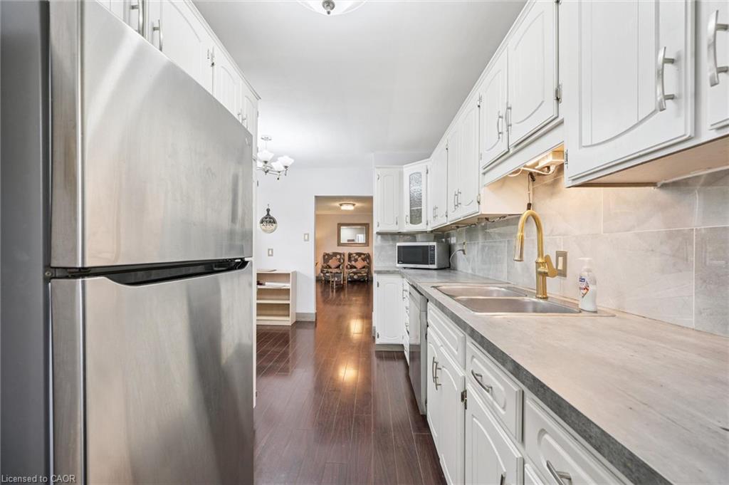 Galley kitchen with white cabinetry, stainless-steel appliances, dark flooring, and a gold-tone faucet.