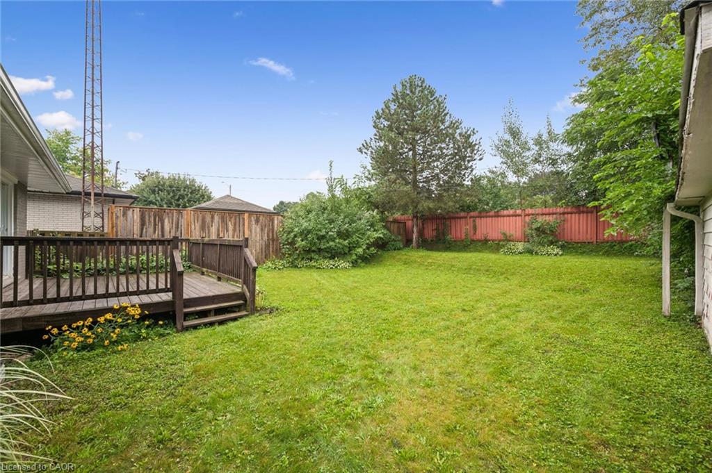 Fenced backyard with a broad lawn, wooden deck, and mature trees.