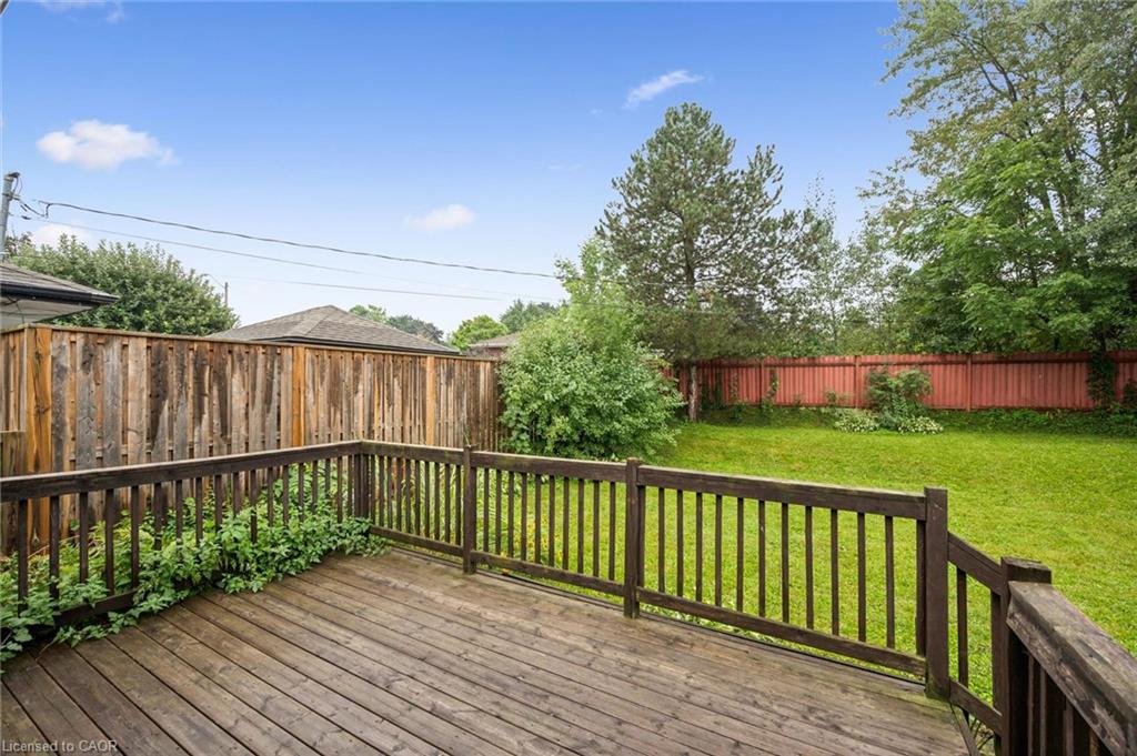Wooden deck overlooking a fenced grassy backyard with mature trees.