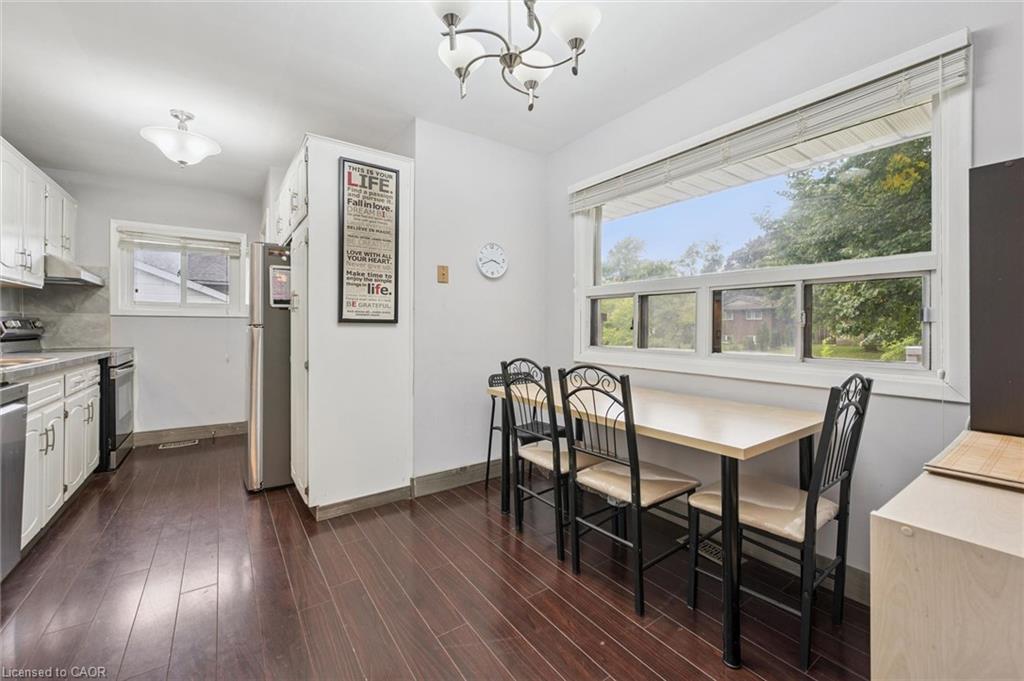 Kitchen with white cabinetry, dark wood floors, and a dining table beside a wide window.
