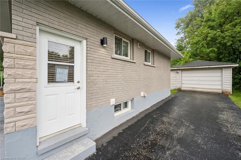 Beige brick house with a white side entrance, paved driveway, and detached garage.