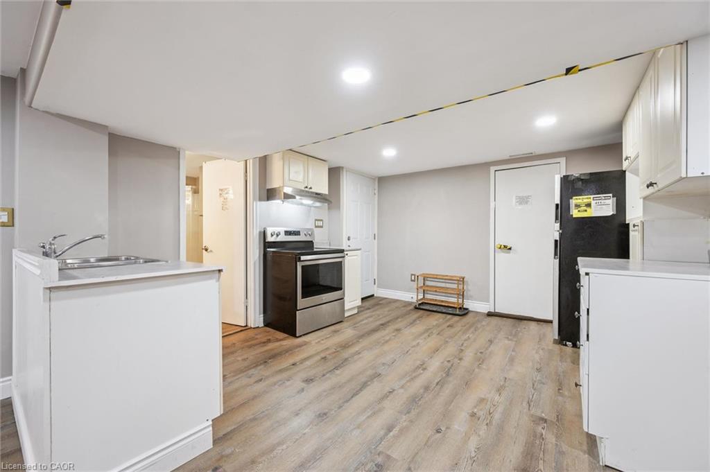 Vacant kitchen with white cabinets, stainless-steel range, black refrigerator, and wood-look flooring.