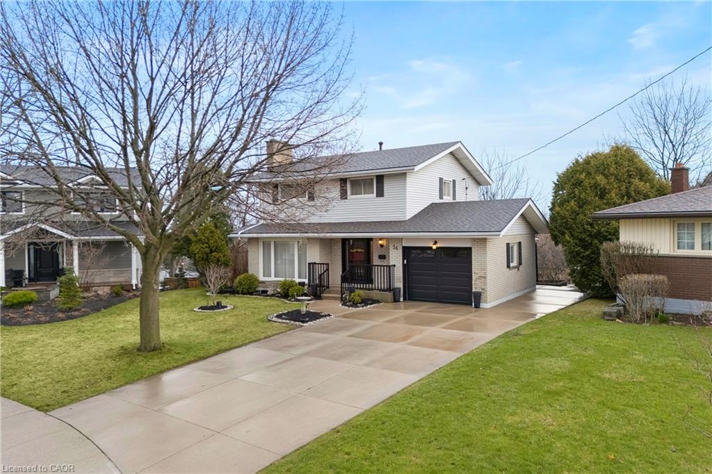 Two-story split-level home with a dark garage, wide driveway, and leafless tree on the lawn.