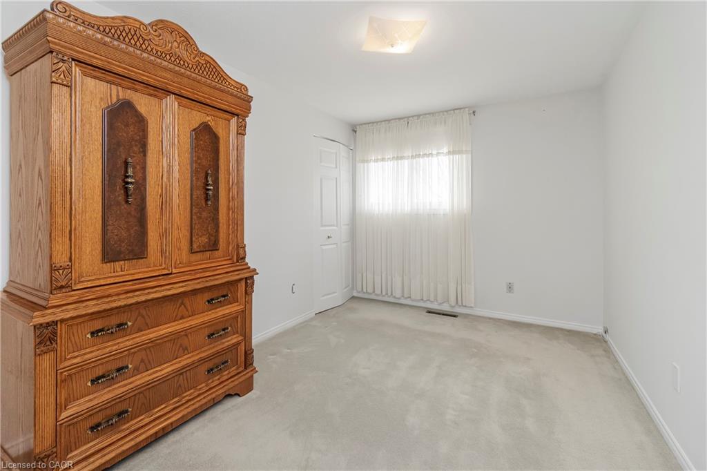 Carpeted bedroom with a large ornate wooden wardrobe and a curtained window.