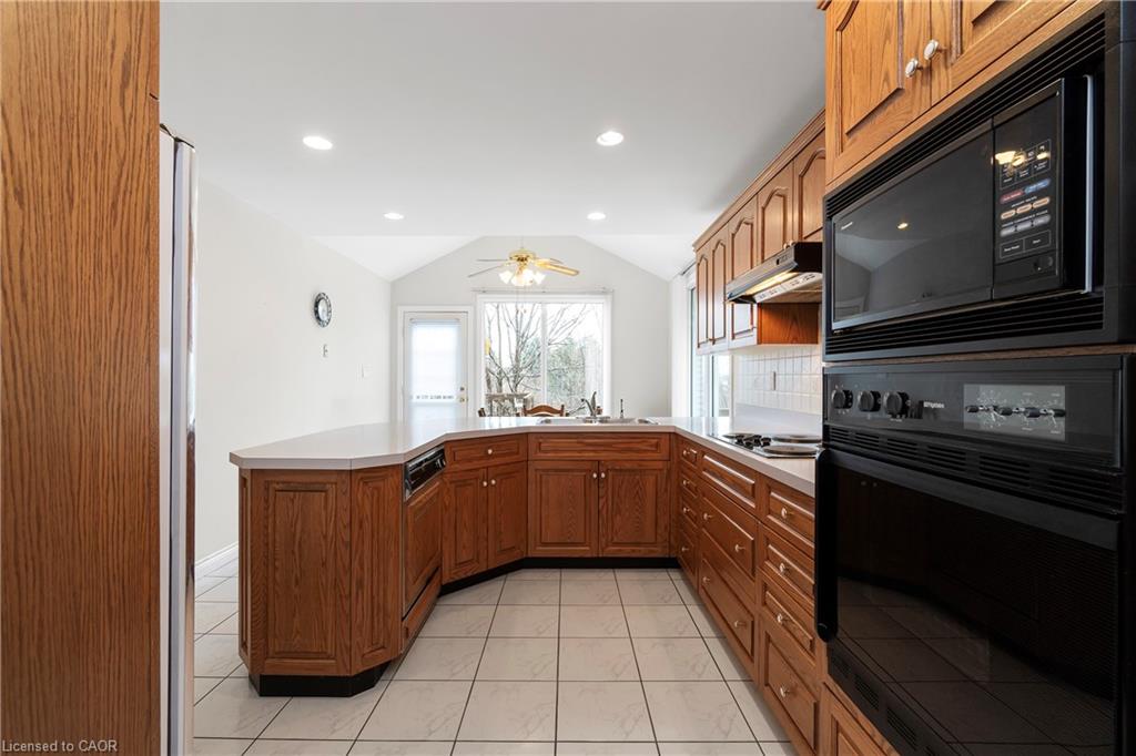 Kitchen with warm wood cabinetry, a peninsula, built-in double oven, and tiled floor.