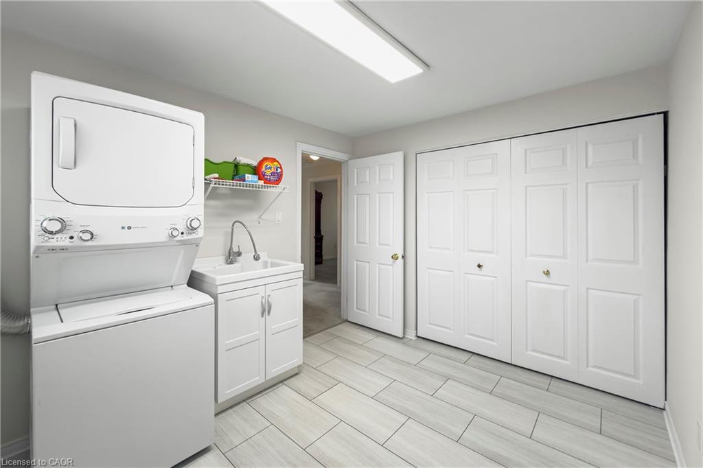 Laundry room with stacked washer and dryer, utility sink, and white built-in cabinets.
