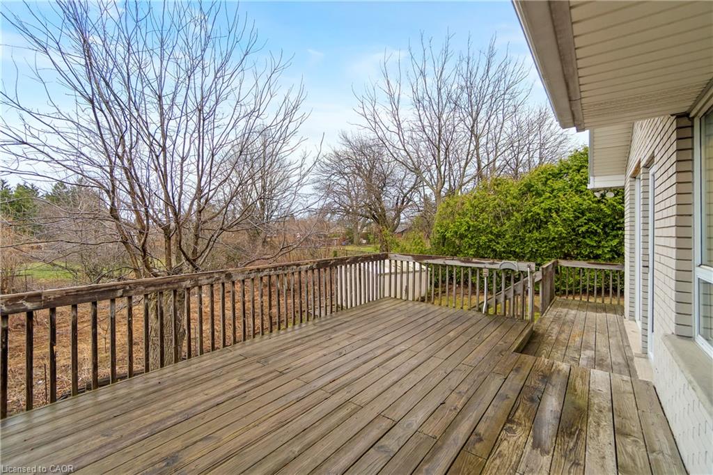 Wooden deck beside a light-sided house, bordered by railings and overlooking leafless trees.