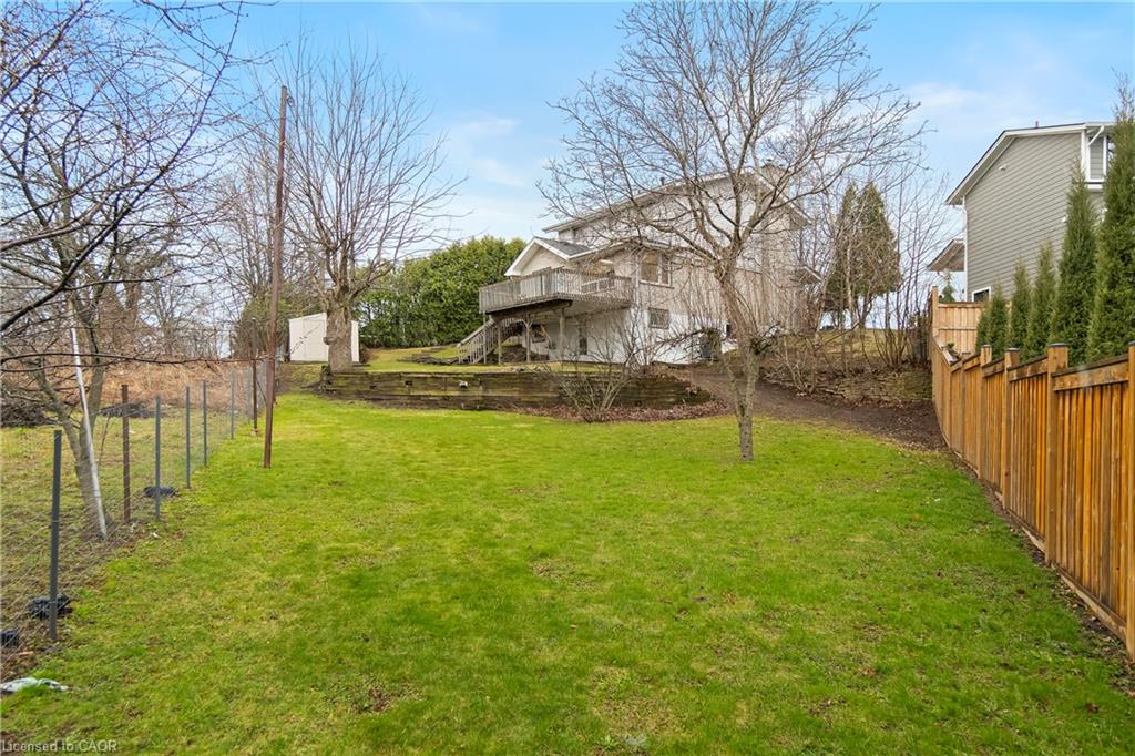 Rear yard with a broad lawn, raised retaining wall, and deck behind the house.
