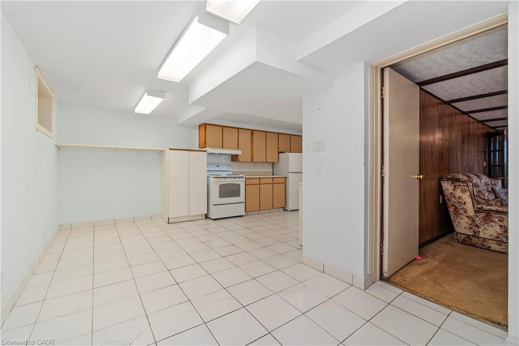 Tiled kitchen with light wood cabinets and white appliances, opening into a wood-paneled sitting room.